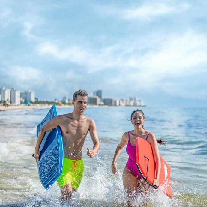 Couple running along the shore with beach body boards in Miami - Visit Florida