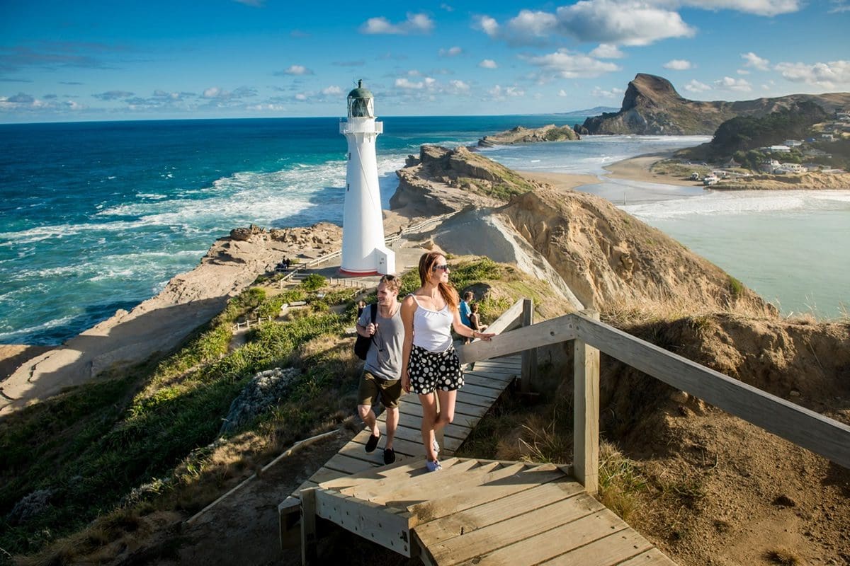 Two people walking up the steps in front of the Castlepoint Lighthouse, Wellington - NZ Tourism